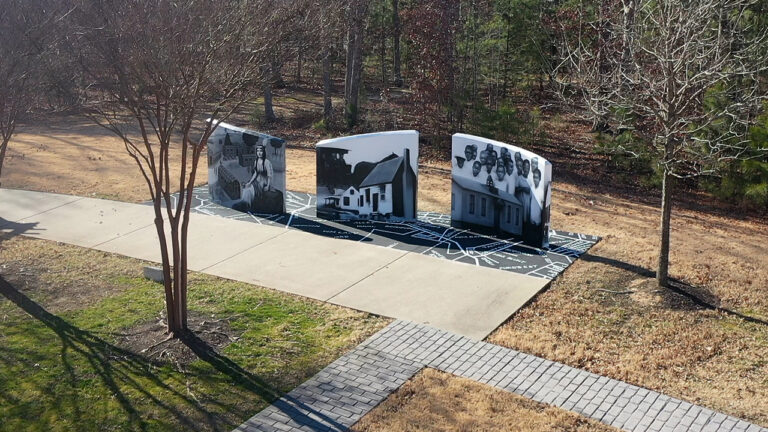 Three concrete walls form a historic mural at a park.