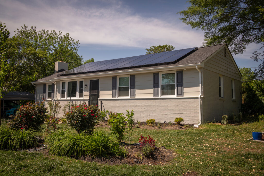 An image of a one story house with a garden in front and solar panels on the roof.