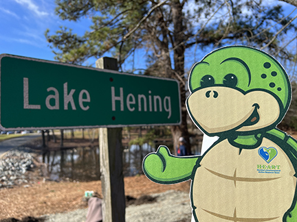 Stewart the turtle mascot cutout next to a green sign with text of Lake Hening