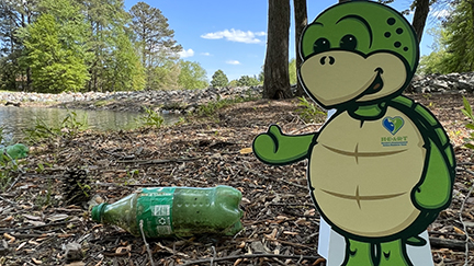 Stewart the turtle mascot cutout next to a plastic green bottle on the ground