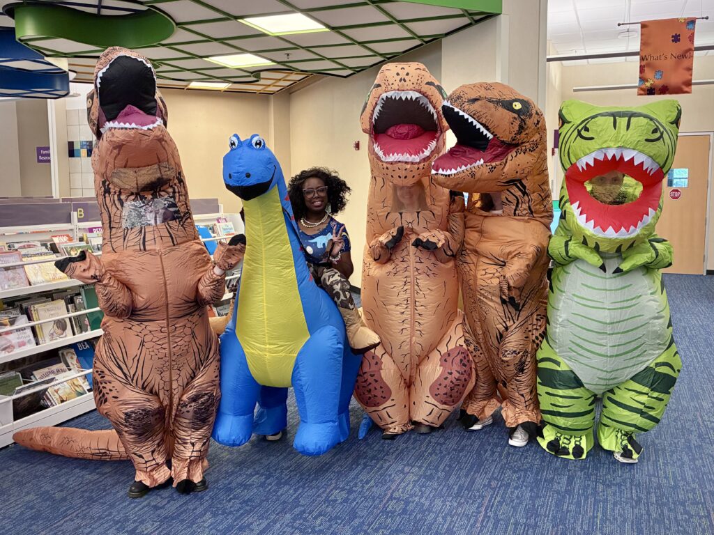 A group of people pose for a photo wearing inflatable dinosaur costumes.