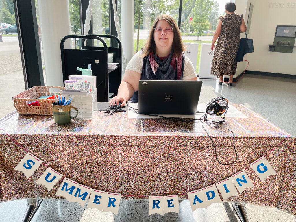 A person sits a table to sign people up for summer reading.