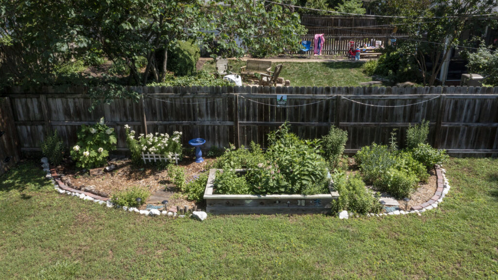 A plot of both in-ground and raised beds of various plants and flowers. A Certified Wildlife Habitat sign hangs on the fence behind the plants.