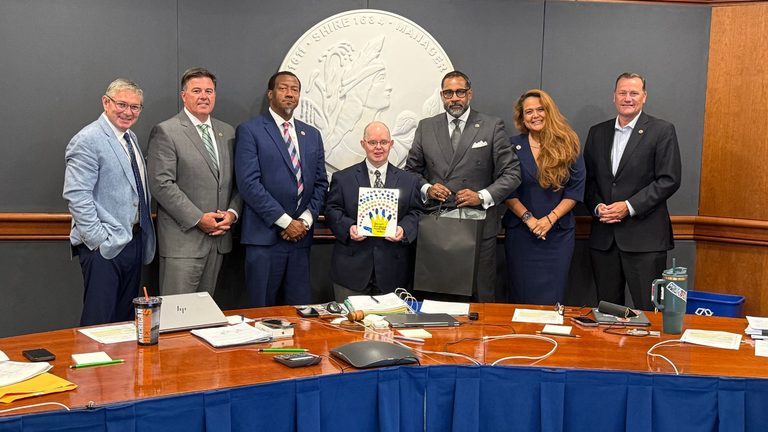 From left to right photo shows: County Manager John Vithoulkas, Tuckahoe District Supervisor Jody Rogish, Varina District Supervisor Tyrone Nelson, Thomas Gardner, who's holding a painting of a hand print that says Down Syndrome Awareness Month, Fairfield District Supervisor and Board Chair Roscoe Cooper, Three Chopt District Misty Roundtree and Brookland District Supervisor Daniel Schmitt.