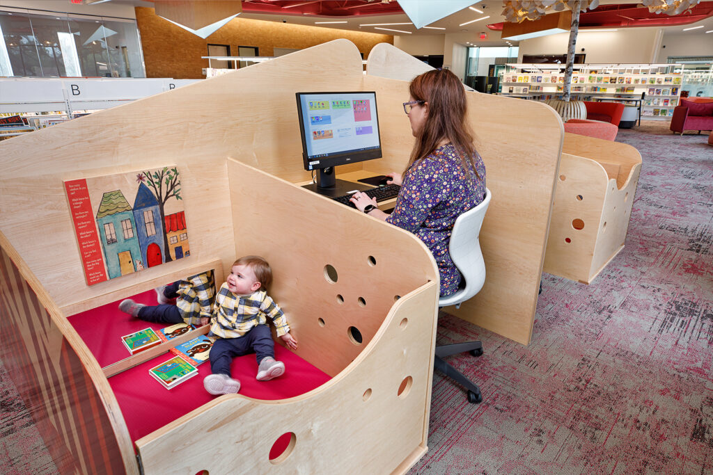 A person works at a desk while their child sits safely in an attached playpen.