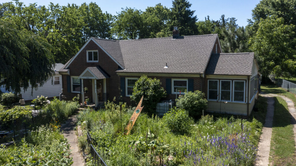 The front yard of home showing minimal, if any, turf grass on the lawn. The yard is full of large flowers, shrubs and other native plants.