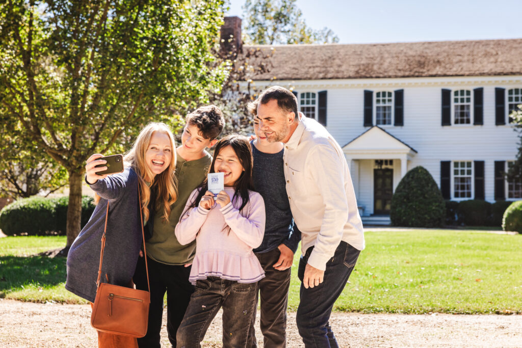 Picture of a family holding the Virginia 250 Passport and taking a selfie in front of a historic building. 