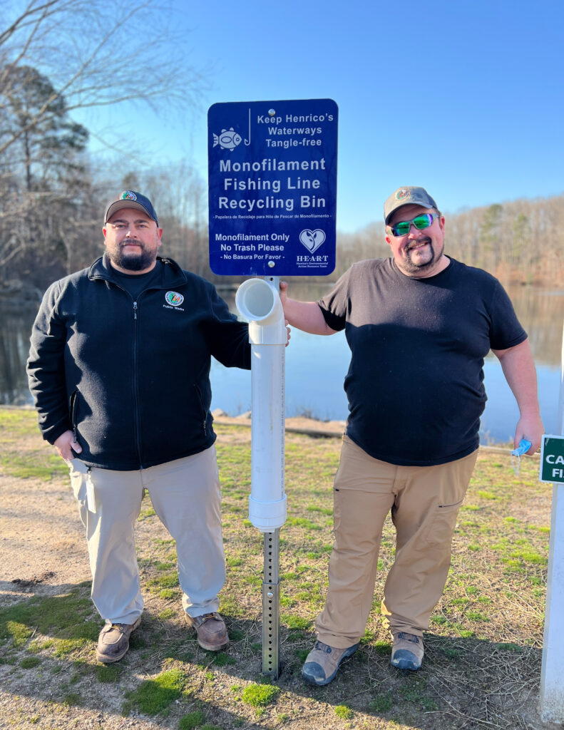 Two men posing next to a fishing line recycling station.