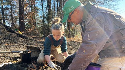 Girl and man planting tree in the dirt.