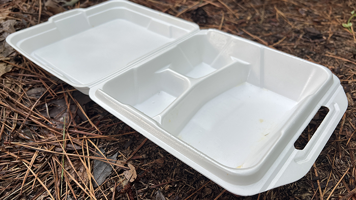 Open Styrofoam carry-out food container on the ground.