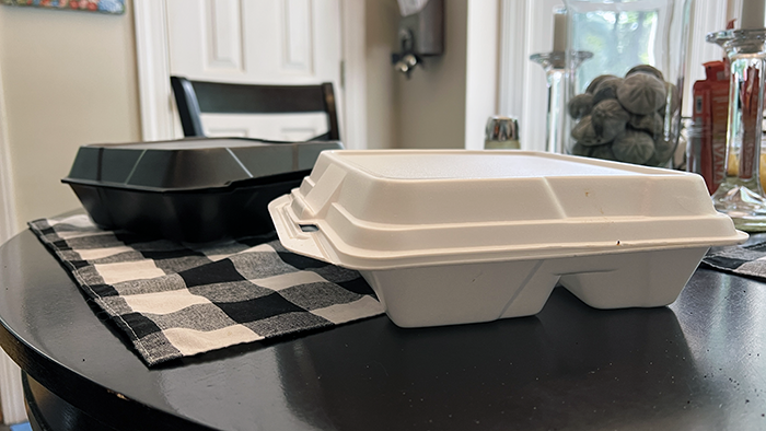 Two Styrofoam food containers on a kitchen table. One white, one black.