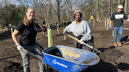 Two women with a wheel barrow and shovel.