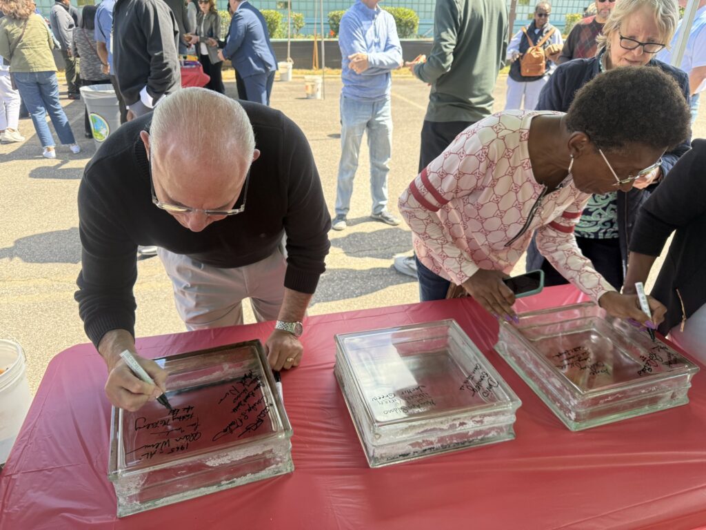 Two people sign glass blocks from a building.