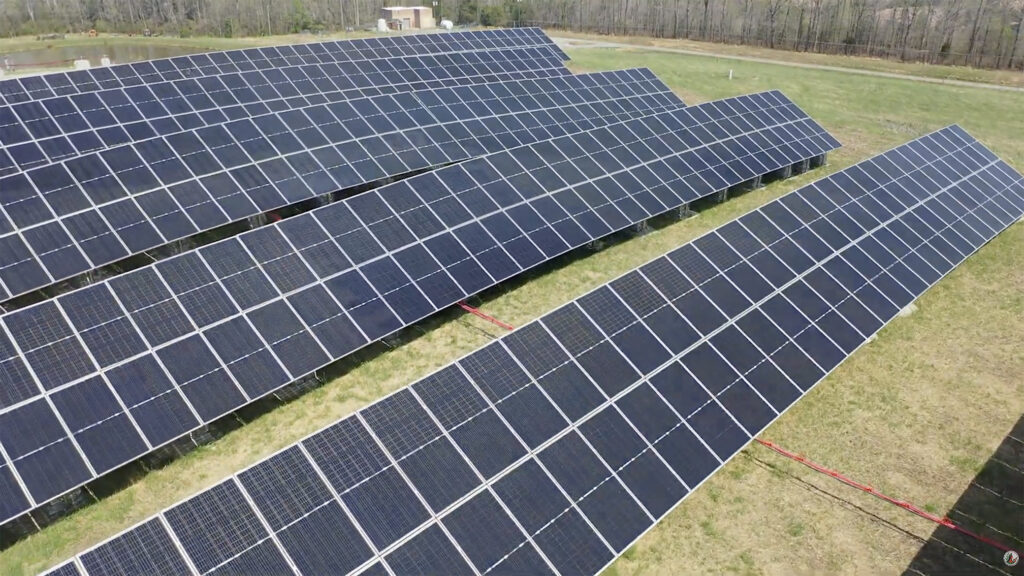 Four horizontal rows of dark solar panels set up in a grassy filed as an array.