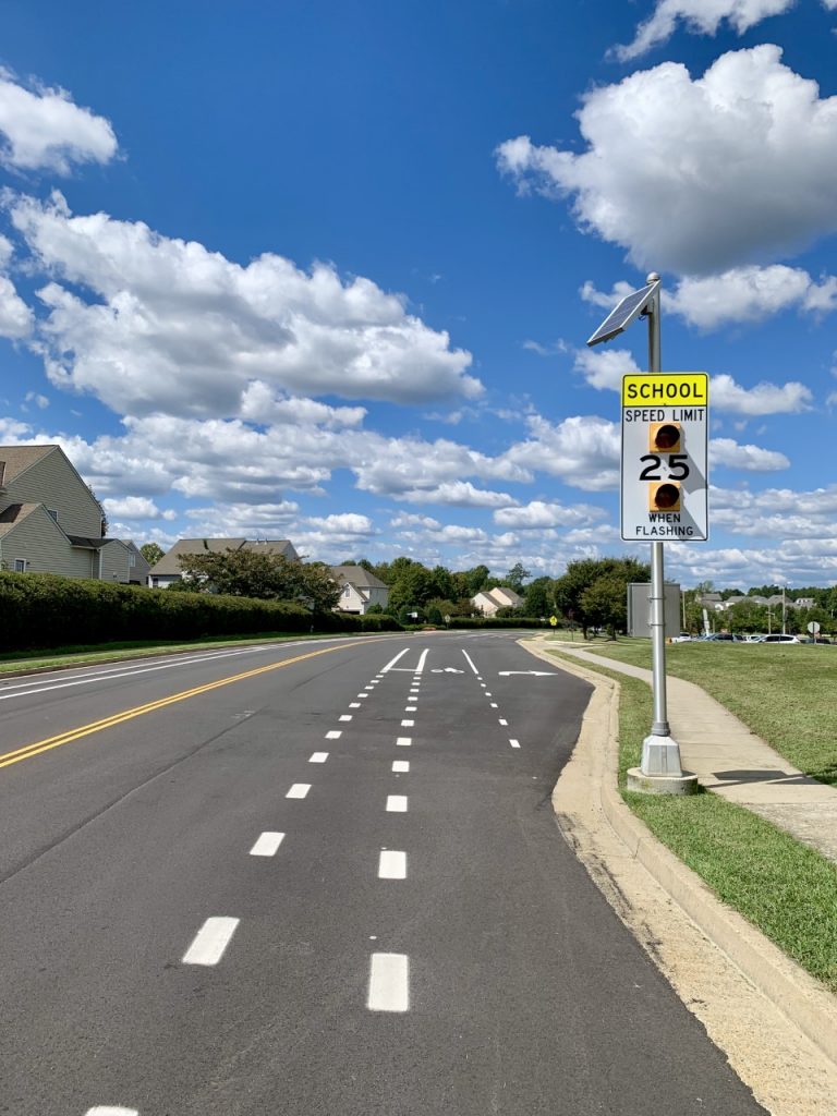 Picture of a roadway with a school zone sign and a striped bike lane.