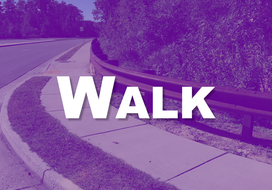 Photo of curved sidewalk with a road on the left and bushes on the right. There is a brown steel barrier between the sidewalk & bushes. Walk is superimposed in white text.