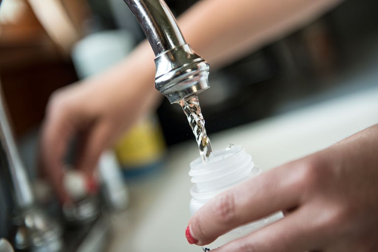 A person fills a bottle with water from a sink.